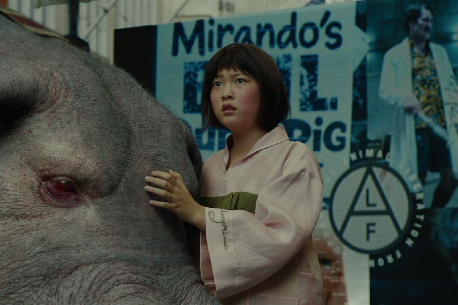 Postać w różowej koszuli trzyma się blisko wielkiego, różowego świniaka w filmie Netflix „Okja”.