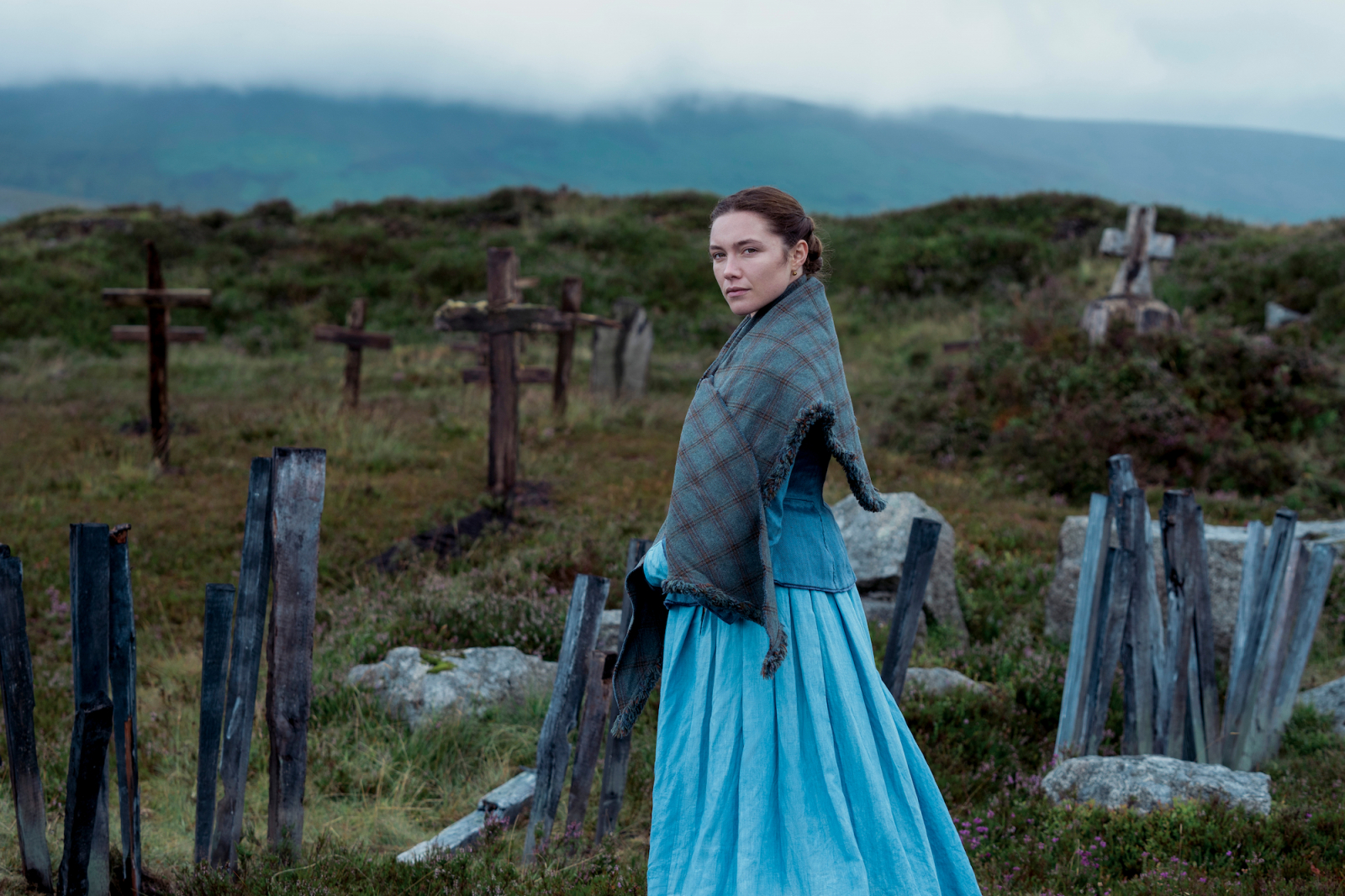 Florence Pugh w filmie Netflix „Osobliwość”, stojąc na tle grobów w malowniczej scenerii.