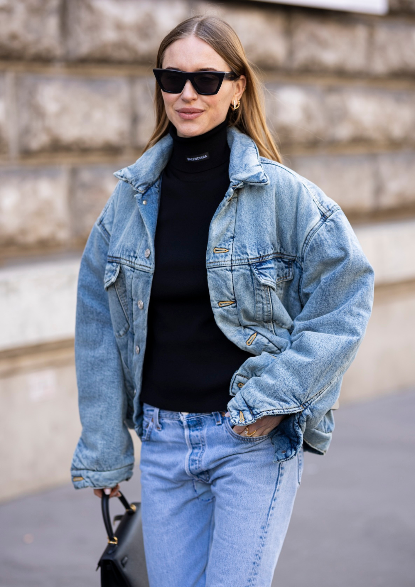 Kobieta w modnym golfie damskim i niebieskich skinny jeans, nosi jeansową kurtkę i okulary przeciwsłoneczne.