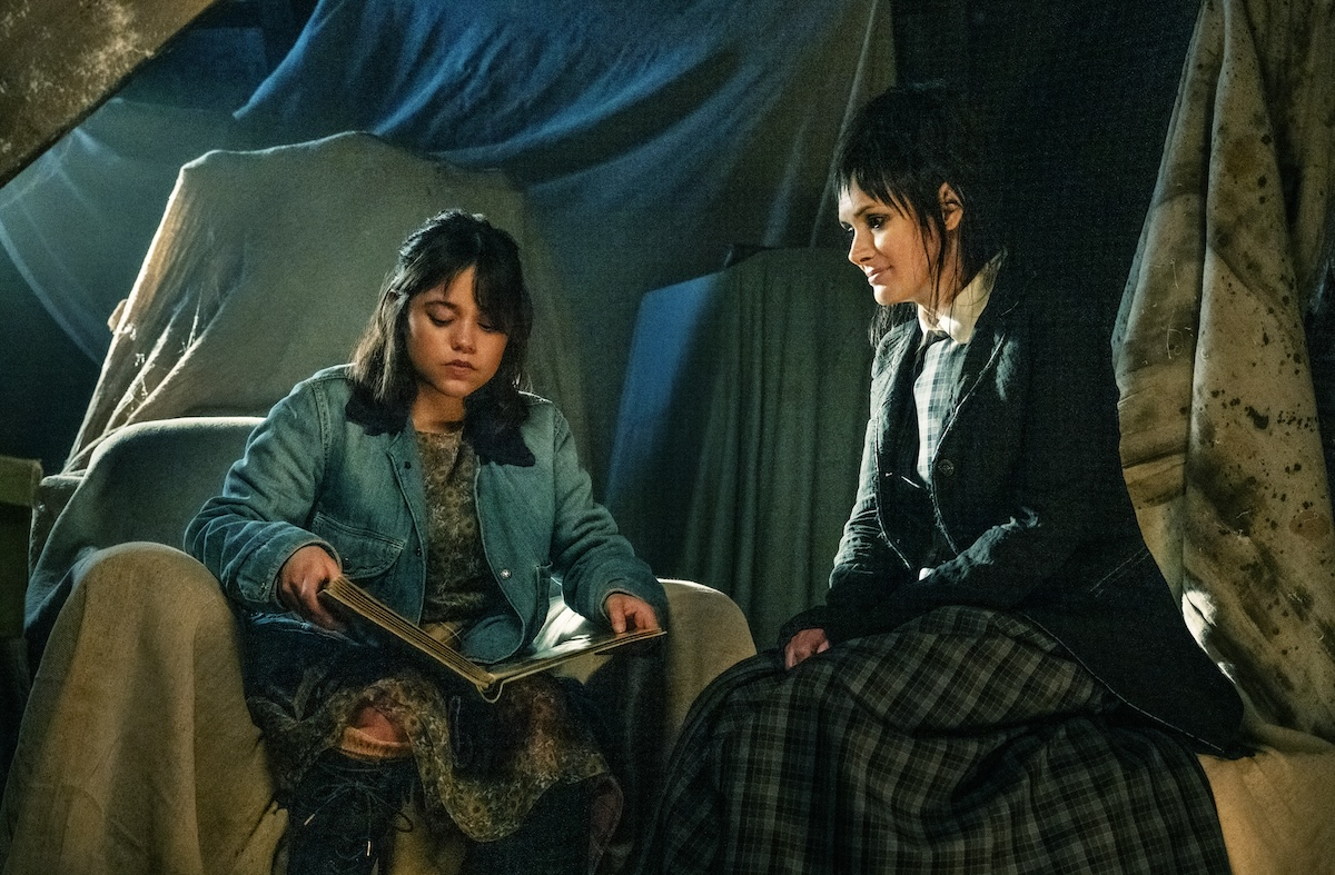 Jenna Ortega i Winona Ryder w filmie "Beetlejuice Beetlejuice", siedzą razem, jedna czyta książkę.