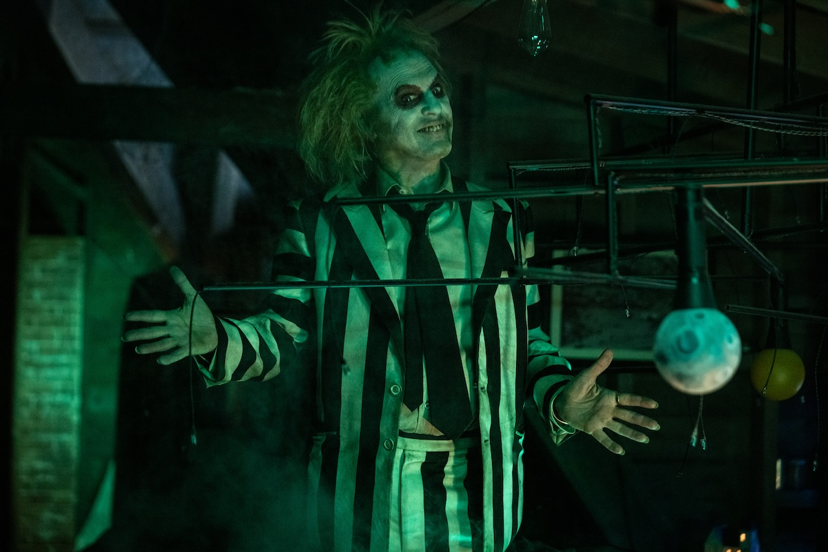 Michael Keaton w prążkowanym garniturze jako Beetlejuice, z charakterystycznym białym makijażem i chaotyczną fryzurą.