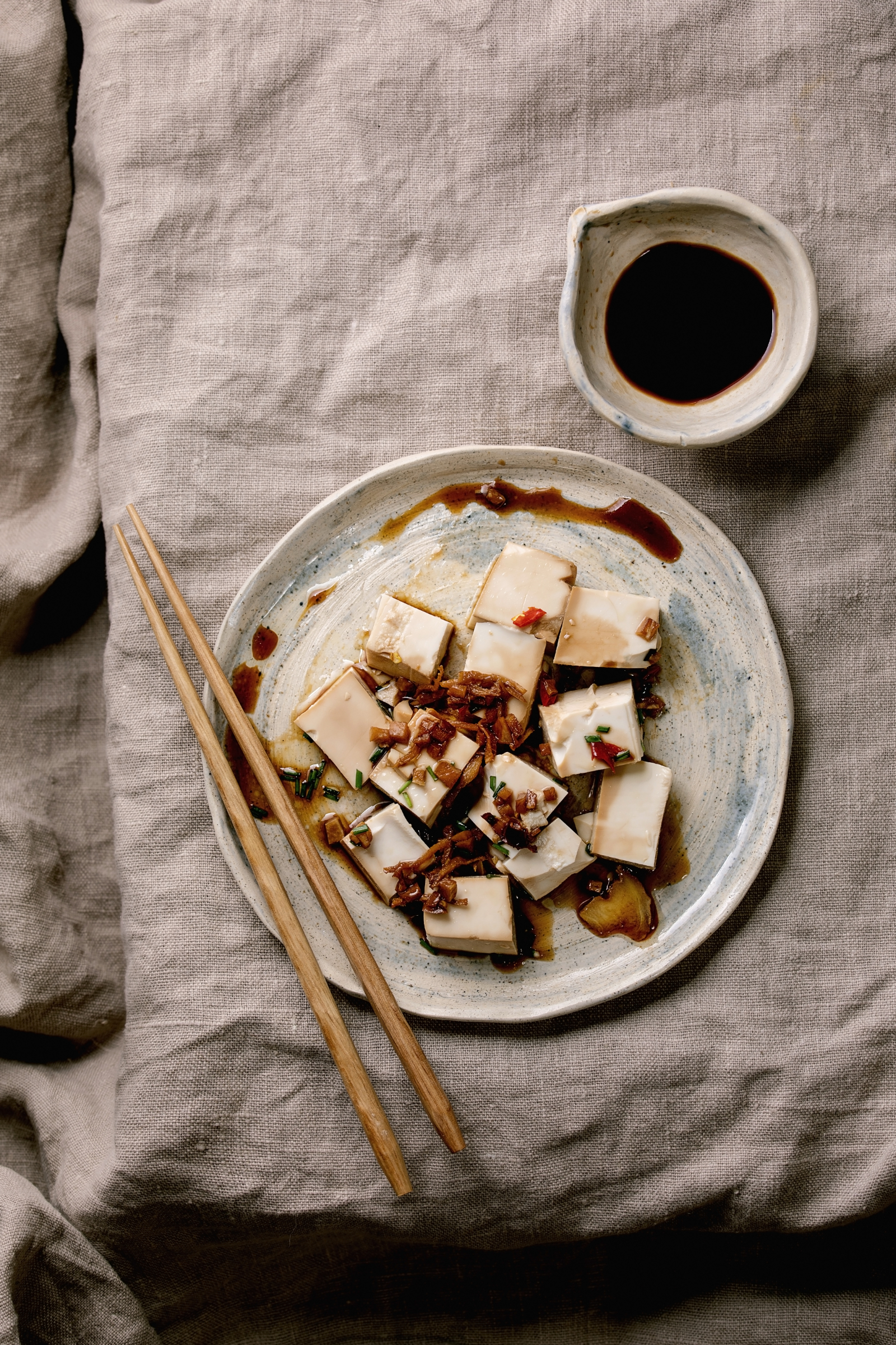 Talerz z tofu pokrojonym w kostkę, posypanym przyprawami, obok sos sojowy i pałeczki.