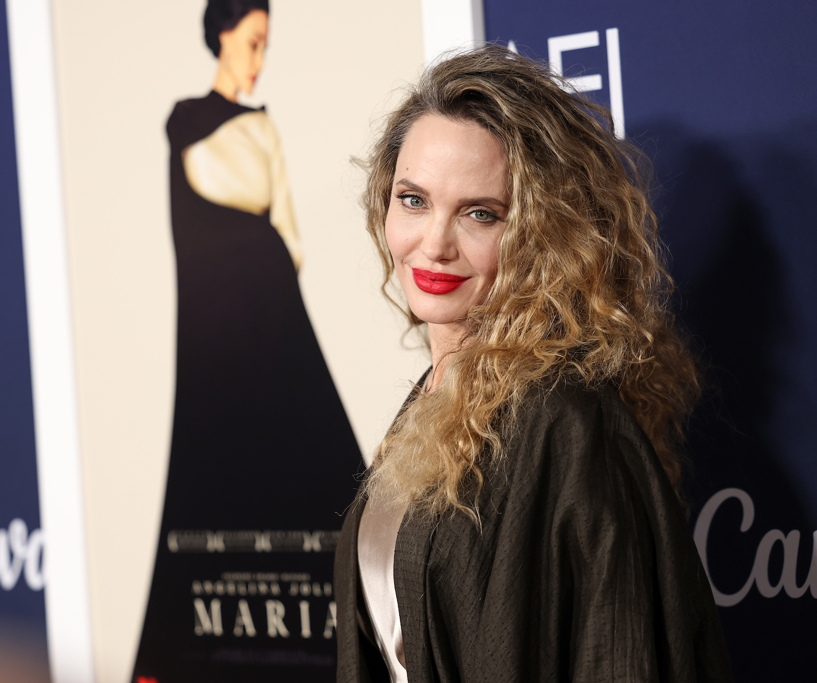 Angelina Jolie, w jedwabnej sukience i z burzą loków, uśmiecha się pozując na tle plakatu filmu "Maria" podczas wydarzenia AFI Fest.