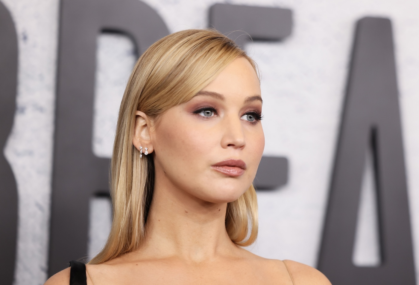Jennifer Lawrence w gładko zaczesanych blond włosach, delikatnym makijaży z subtelnie podkreślonymi ustami.