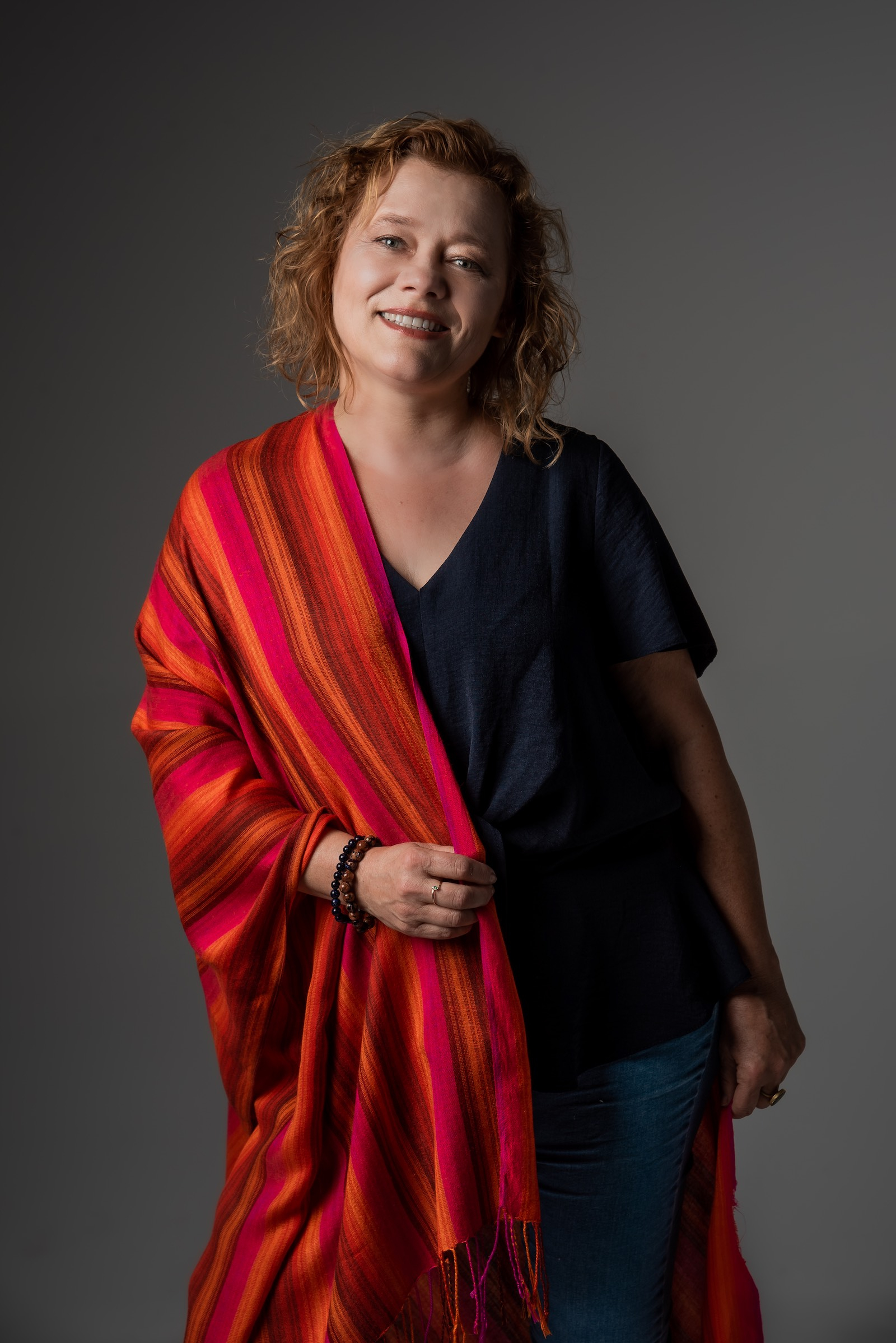 Karin Lesniak, trenerka śmiechu, pozuje do zdjęcia w ciemnej bluzce i dżinsach, trzymając na ramionach czerwony szal.