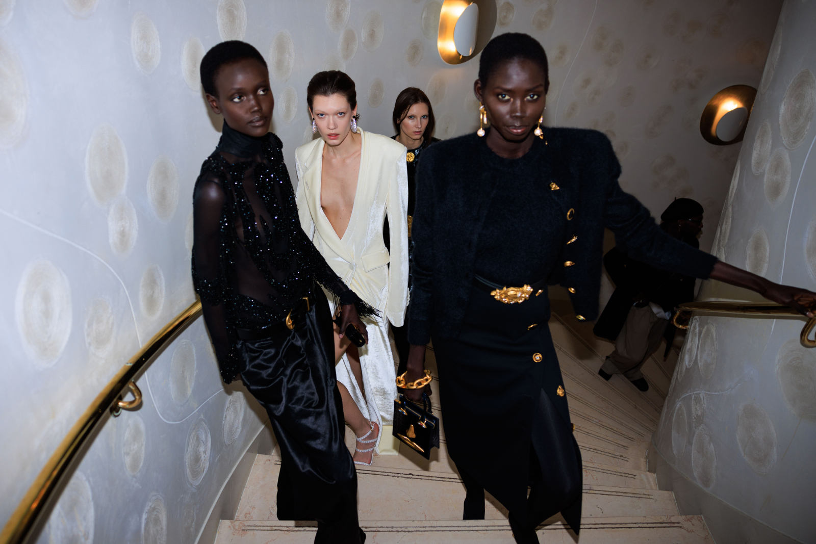 Modelki w eleganckich kreacjach Schiaparelli schodzą po schodach w stylowym wnętrzu.