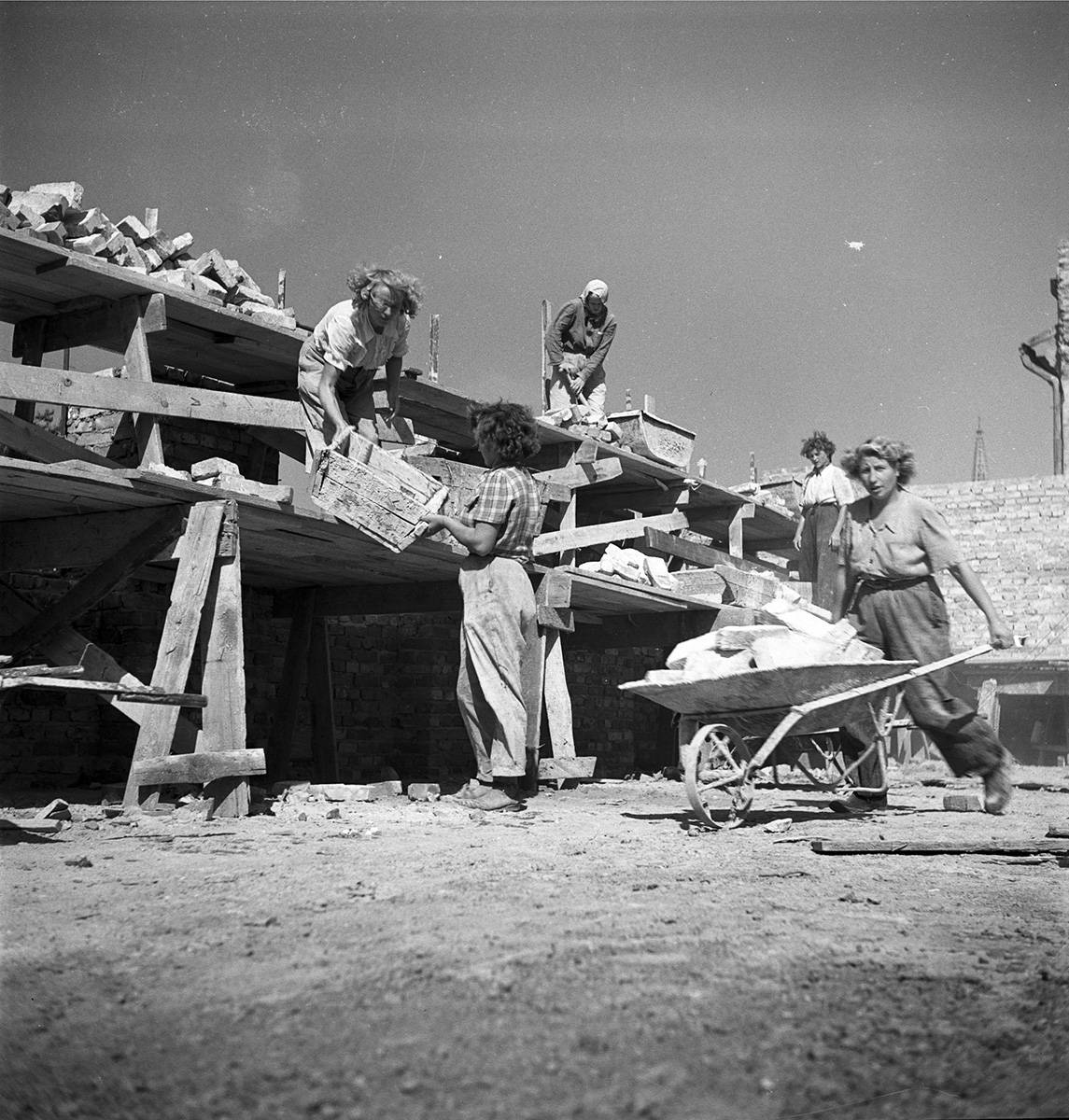 3)Brygada kobieca budująca blok mieszkalny. Widoczna robotnica przewożąca cegły na taczkach, fot. Siemaszko Zbyszko, NAC