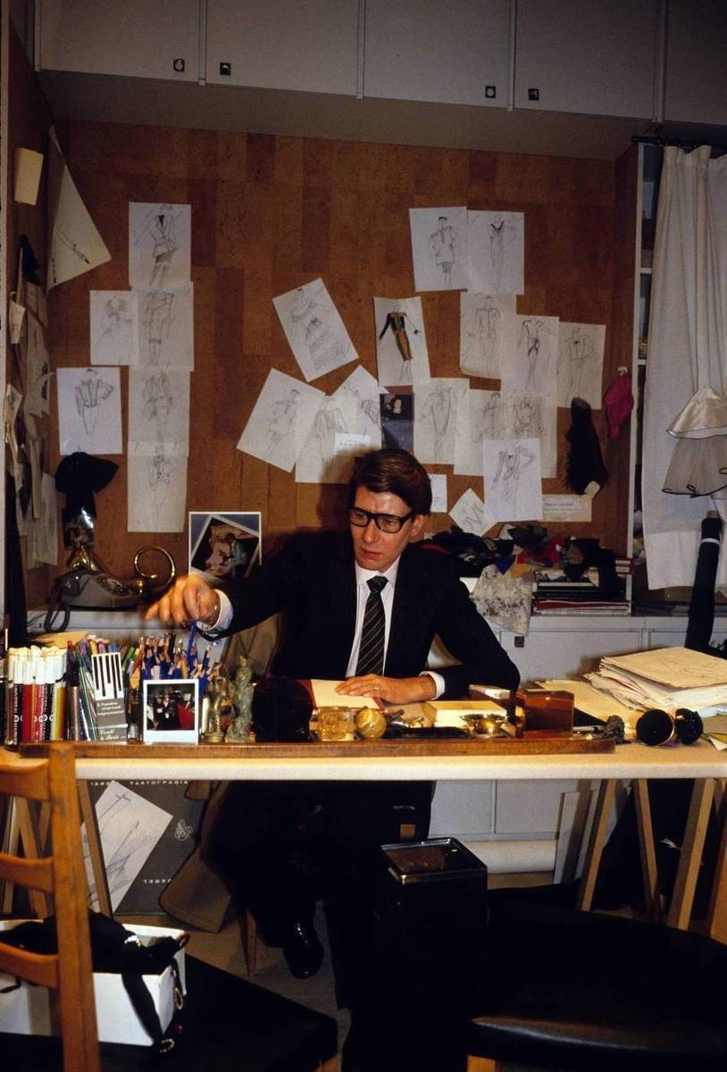 Projektant Yves Saint Laurent pracujący przy biurku w otoczeniu swoich szkiców.