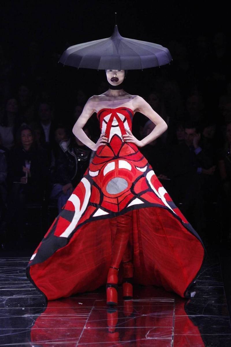 Modelka idąca na wybiegu u Alexandara McQueena w obszernej sukni z kolekcji  jesień-zima 2009/2010. Na głowie ma ogromny kapelusz i nieproporcjonalnie duże, czerwone usta.